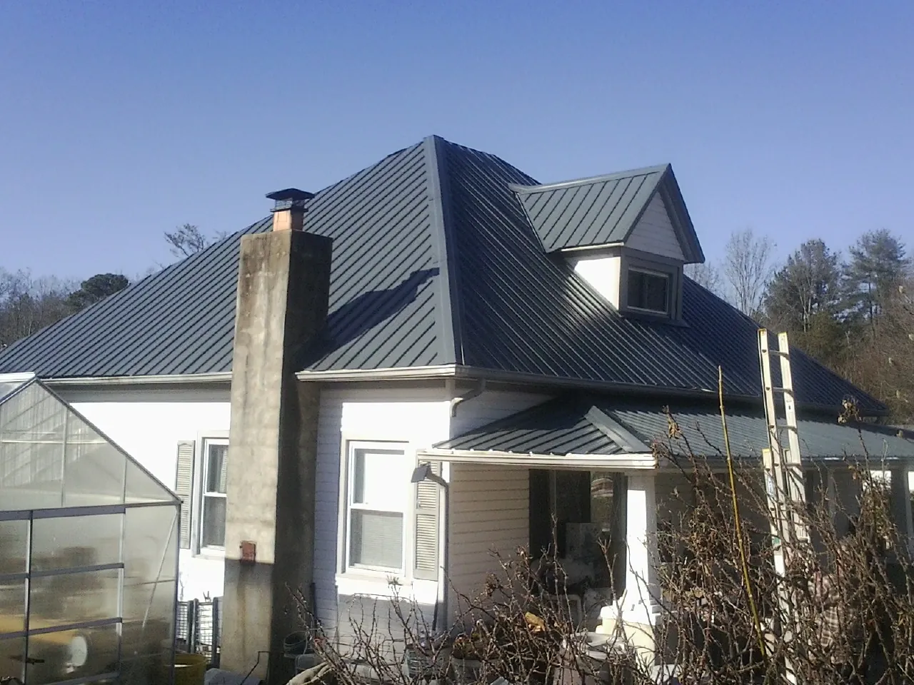 Dark blue standing seam metal roof on a white farmhouse with dormer — Slate & Tile Roof Repair by Roofing Brothers in Kearny