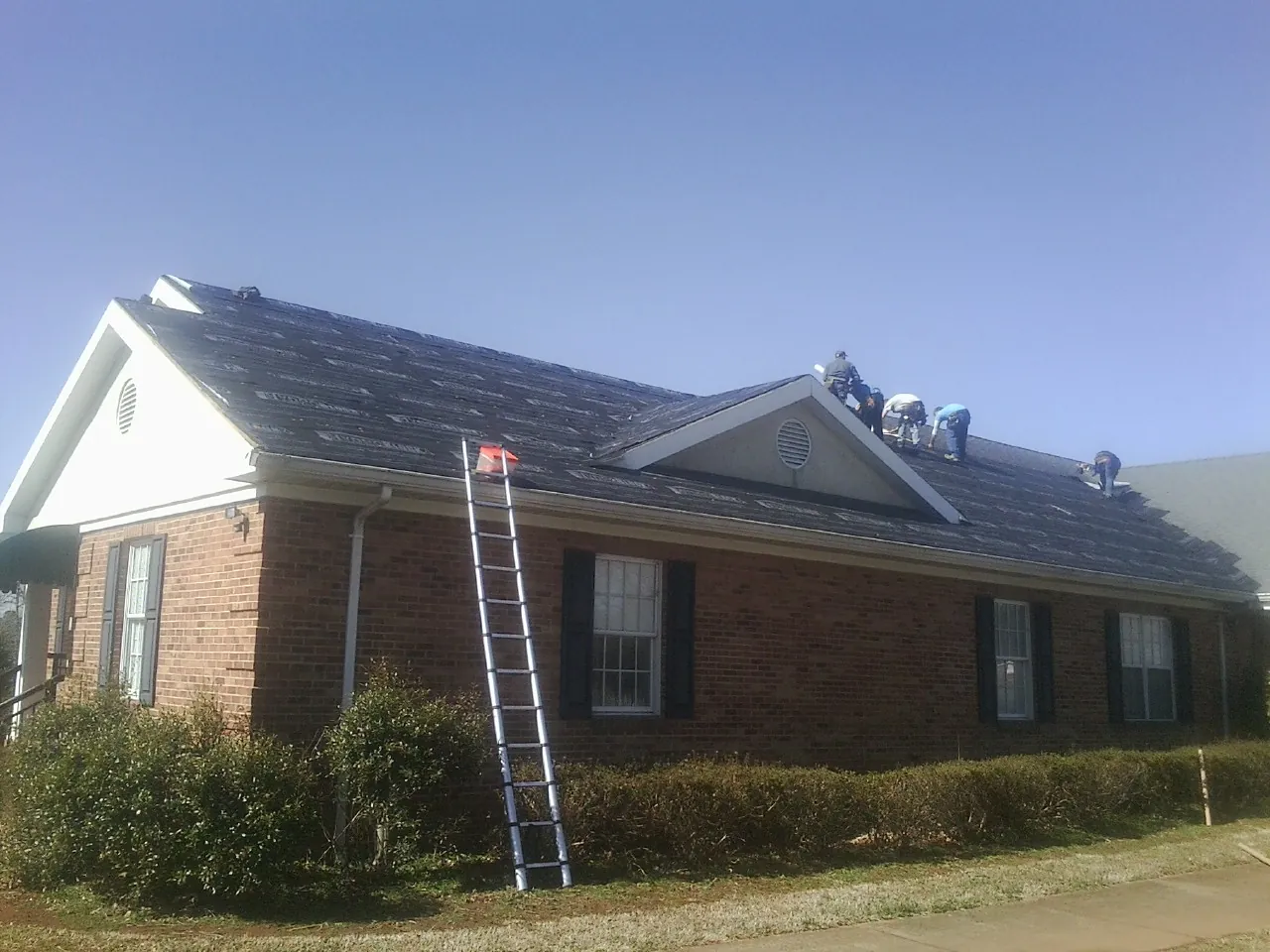 Crew tearing shingles off a brick ranch roof with a ladder set — Emergency Roof Repair work by our crew in Kearny