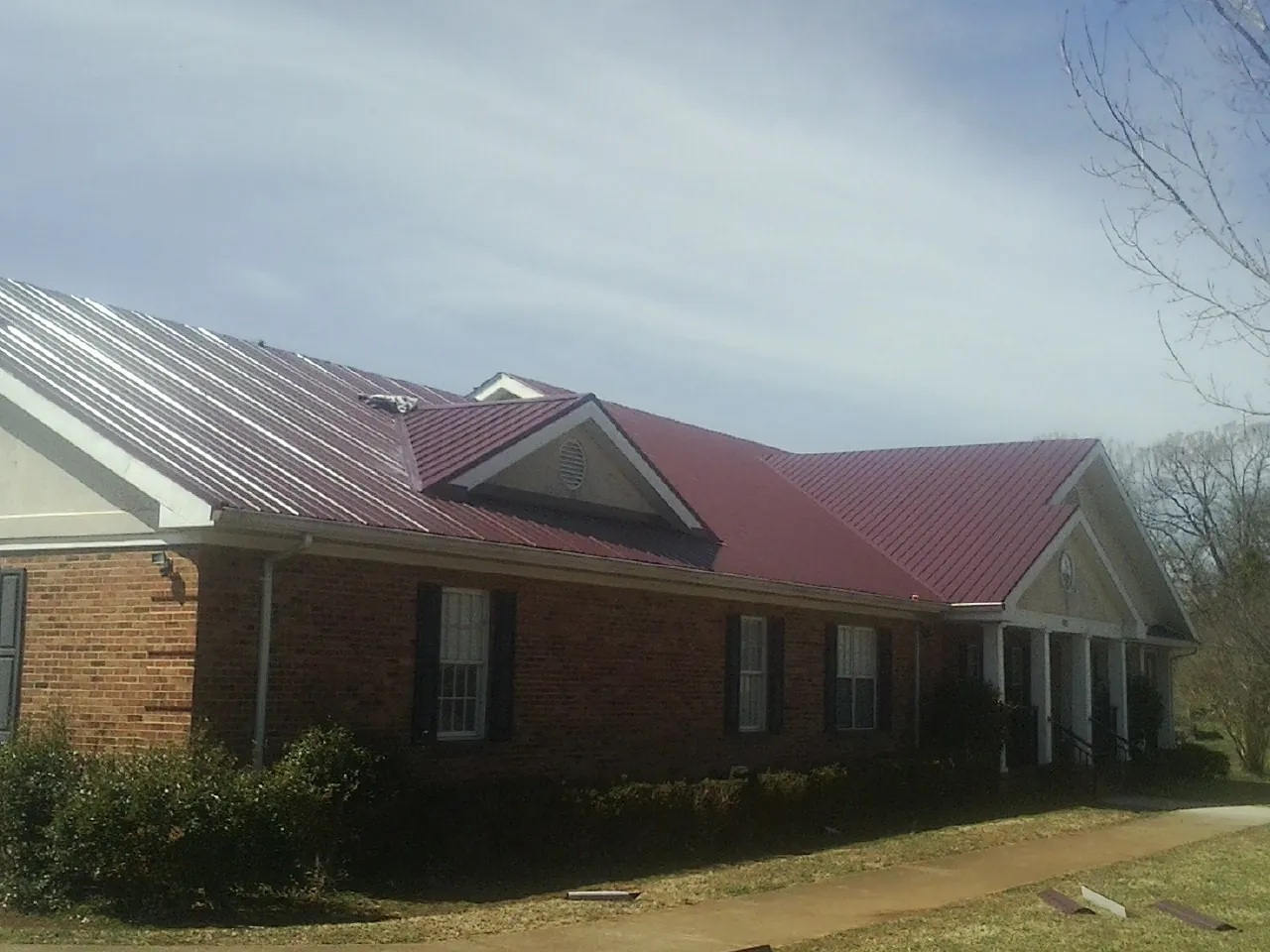 Red metal roof with gabled entries on a long brick building, from a Hail Damage Roof Repair job in Kearny