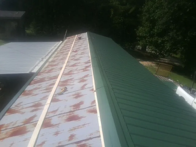 Old rusted panels beside newly installed green metal roofing — Wind Damage Roof Repair by Roofing Brothers in Kearny