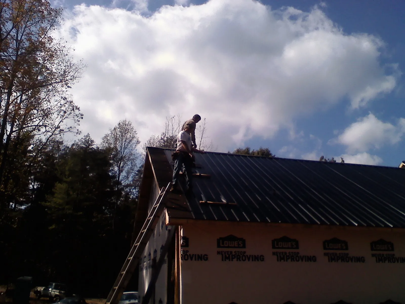 Roofer fastening dark metal panels high against a cloudy sky, from a Roof Inspection job in Kearny