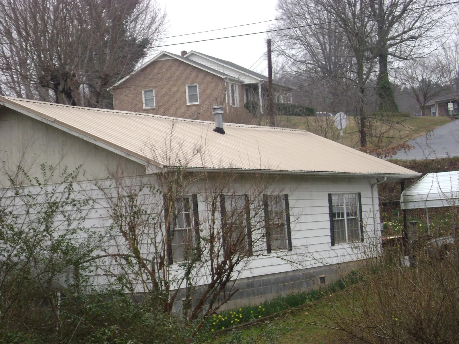 Tan metal roof on a white sided house set into a hillside — Commercial Roofing by Roofing Brothers in Kearny