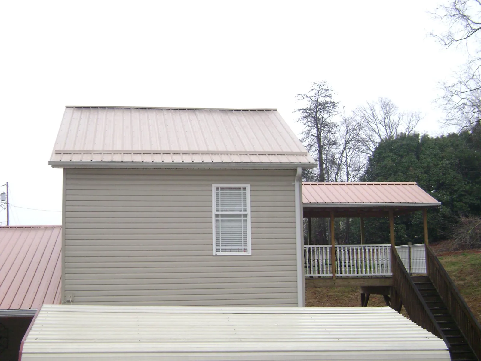 Tan metal roofs on a two story addition and attached porch, from a Roof Replacement job in Kearny